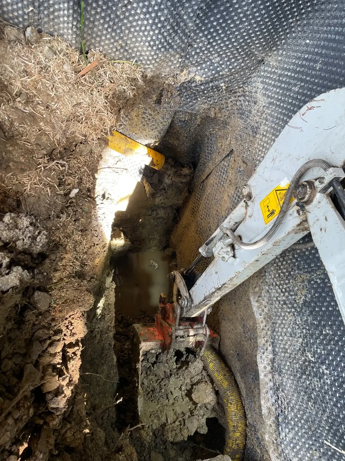 Odkopane ściany fundamentowe z widoczną wodą i uszkodzonym drenażem