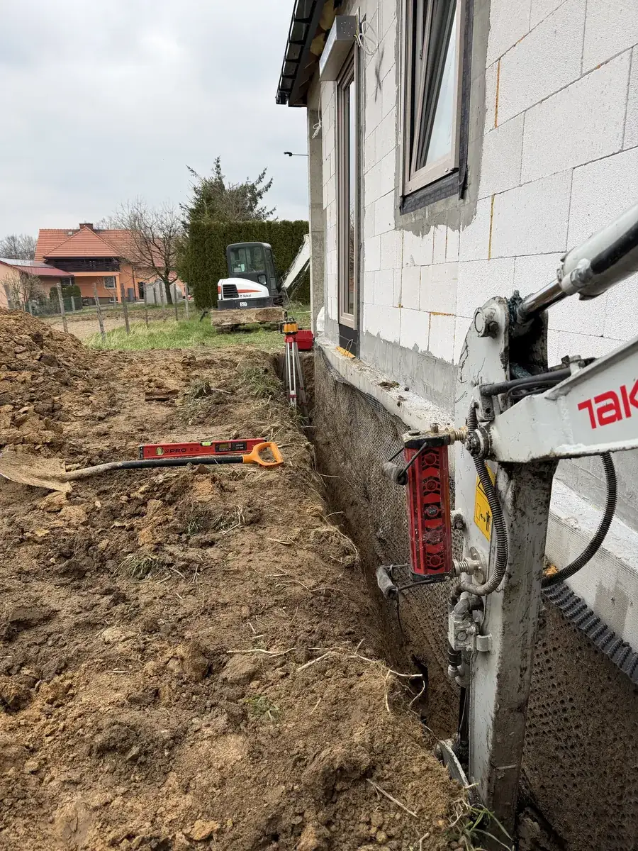Kontrola głębokości wykopu niwelatorem laserowym – odbiornik na ramieniu minikoparki, w tle Bobcat E50