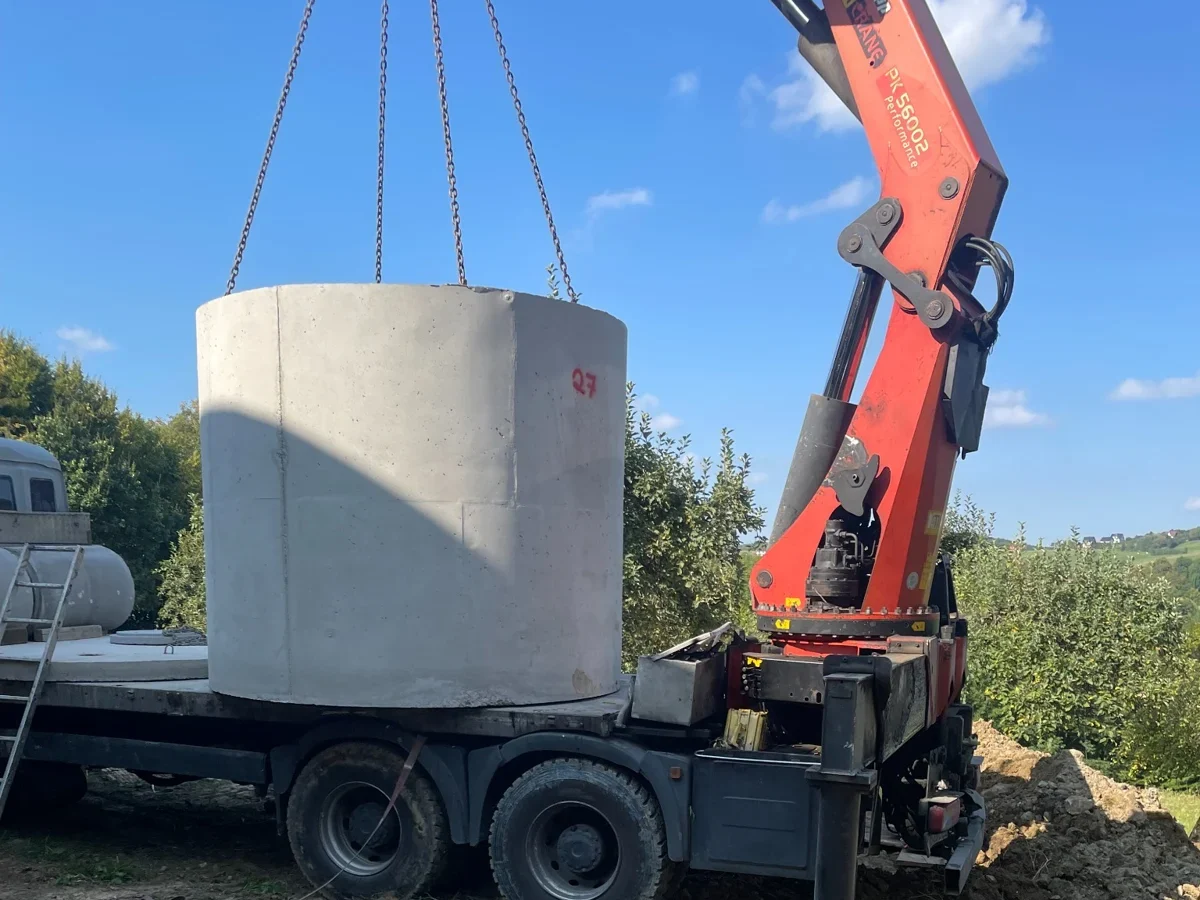Dźwig HDS osadza betonowy zbiornik na deszczówkę podczas naprawy odwodnienia domu - RentBud