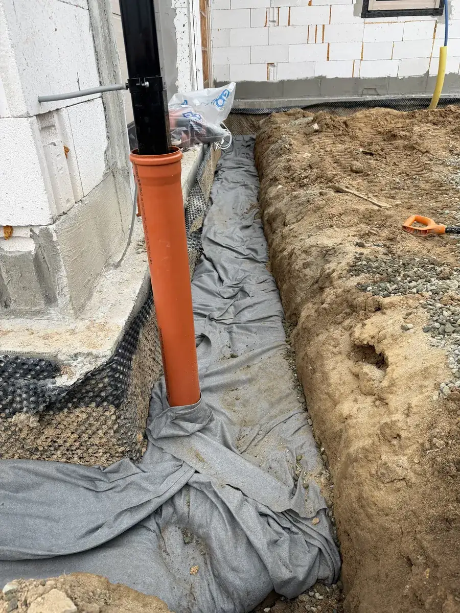 Rura spustowa wprowadzona do rury PVC, obok przygotowany drenaż opaskowy w geowłókninie