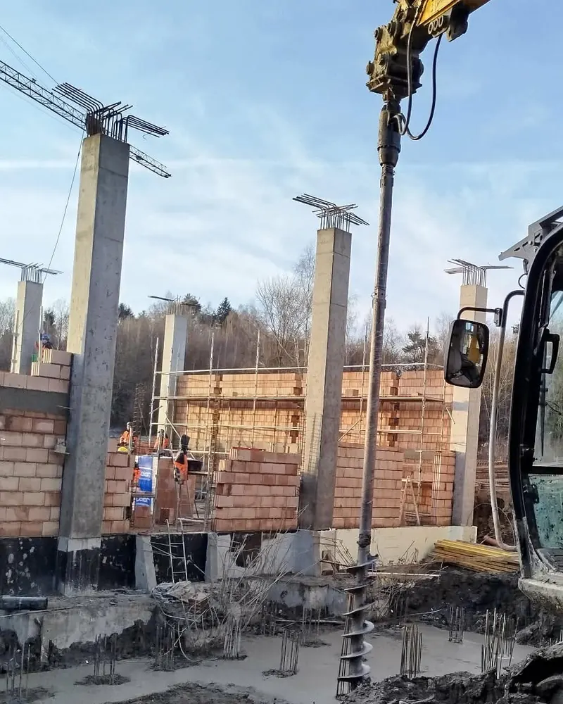 Koparka JCB 25 t ze świdrem podczas wiercenia otworu pod pal fundamentowy na budowie